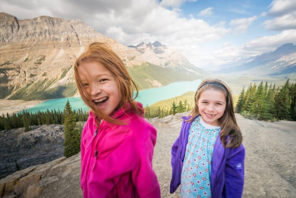 Two children pose in front of the turquoise waters of Peyto Lake, surrounded by Canadian Rockies mountains and evergreen forests.