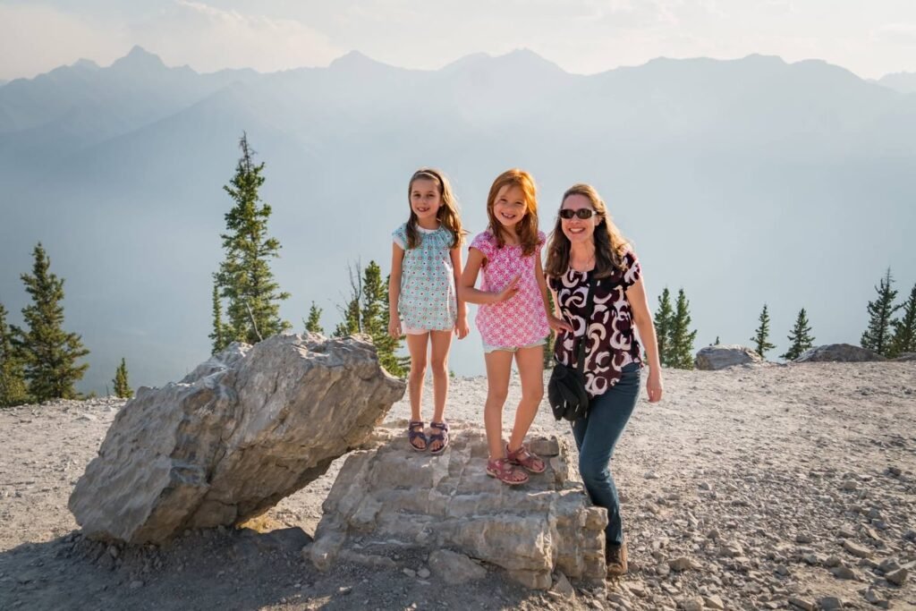 A family poses on rocks at a mountain summit with misty peaks and evergreen trees.