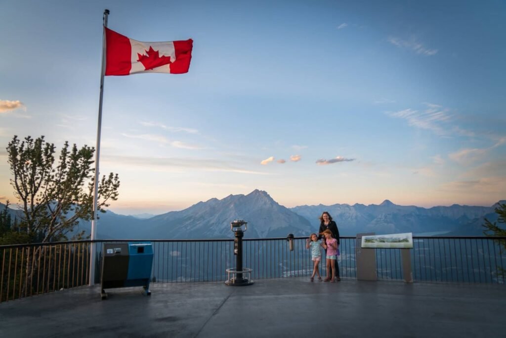 A scenic overlook in Squamish features a Canadian flag flying against a backdrop of mountain peaks and a twilight sky. Visitors enjoy the stunning coastal view from the observation deck.