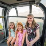 Smiling family posing inside a glass-windowed gondola with a view of mountain scenery.