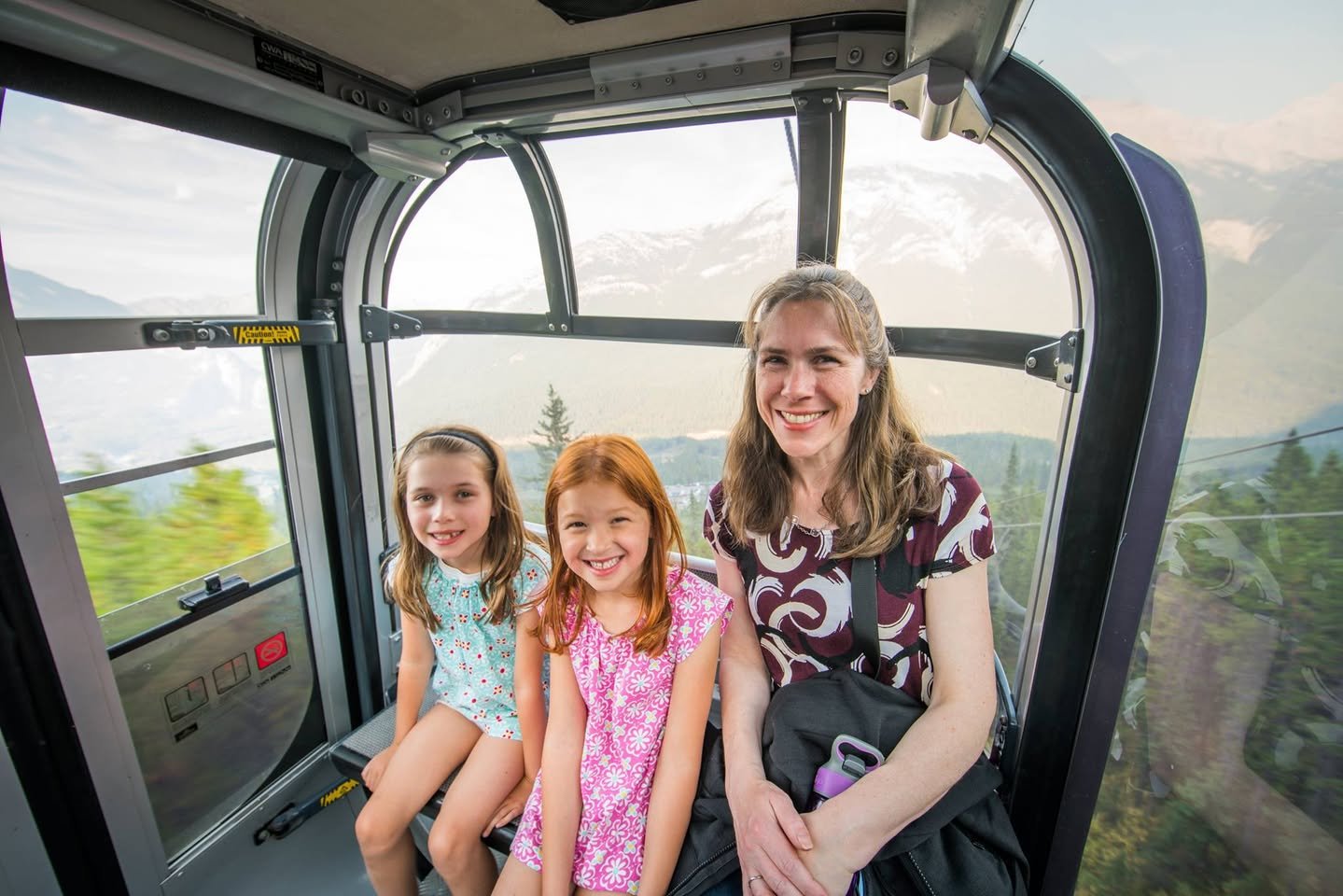 Banff Gondola Smiling family posing inside a glass-windowed gondola with a view of mountain scenery.