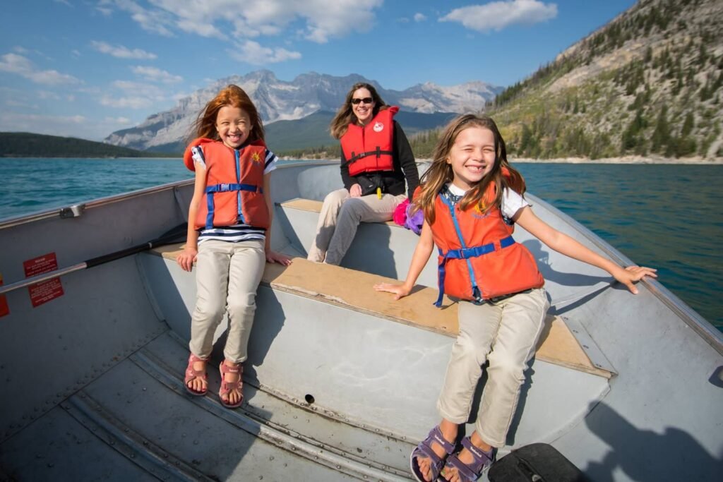 People wearing orange life jackets enjoy a boat ride on a calm alpine lake with mountains.
