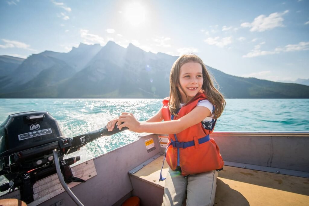 A person in an orange life jacket practices steering a boat. The view includes a Tohatsu engine and scenic mountains.