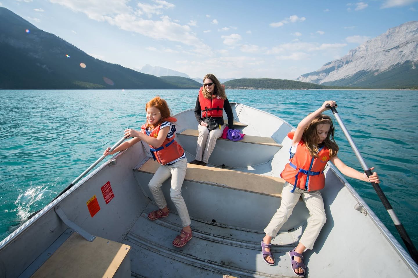Lake Minnewanka A collage of photos showing people wearing life jackets rowing a boat on turquoise water with mountains in the background.