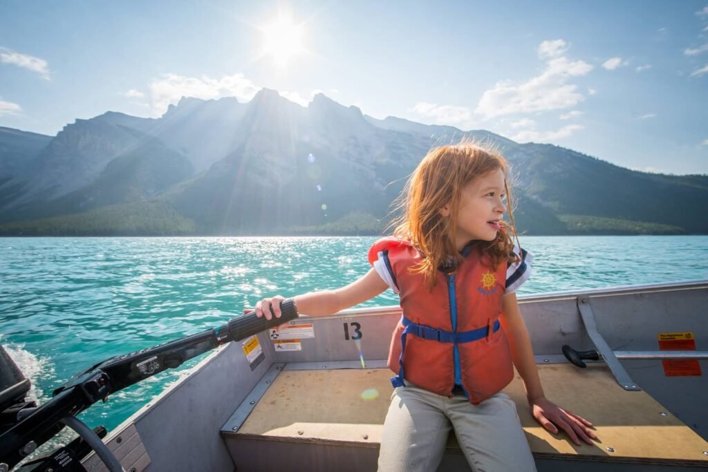 A traveler wearing an orange life vest enjoys a boat ride on turquoise waters with mountainous backdrops under bright sunshine.