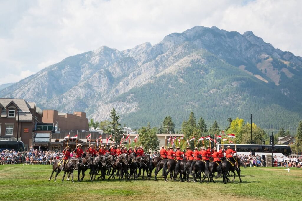 Police officers on horseback perform in a street parade in Banff, Manitoba with a large crowd watching from the sidewalks.