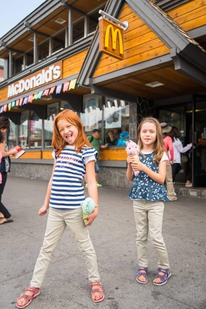 Two children enjoy ice cream in front of a wooden McDonald's restaurant. The building features a mix of modern and rustic architectural styles.