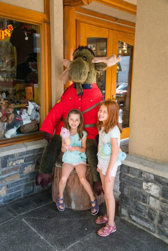 Two girls standing outside a store, one sitting on a bear mascot's lap with ice cream.