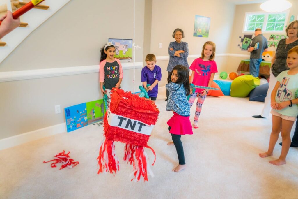 Children gather around a TNT piñata for a fun party activity. Colorful streamers scatter on the floor after the hit.