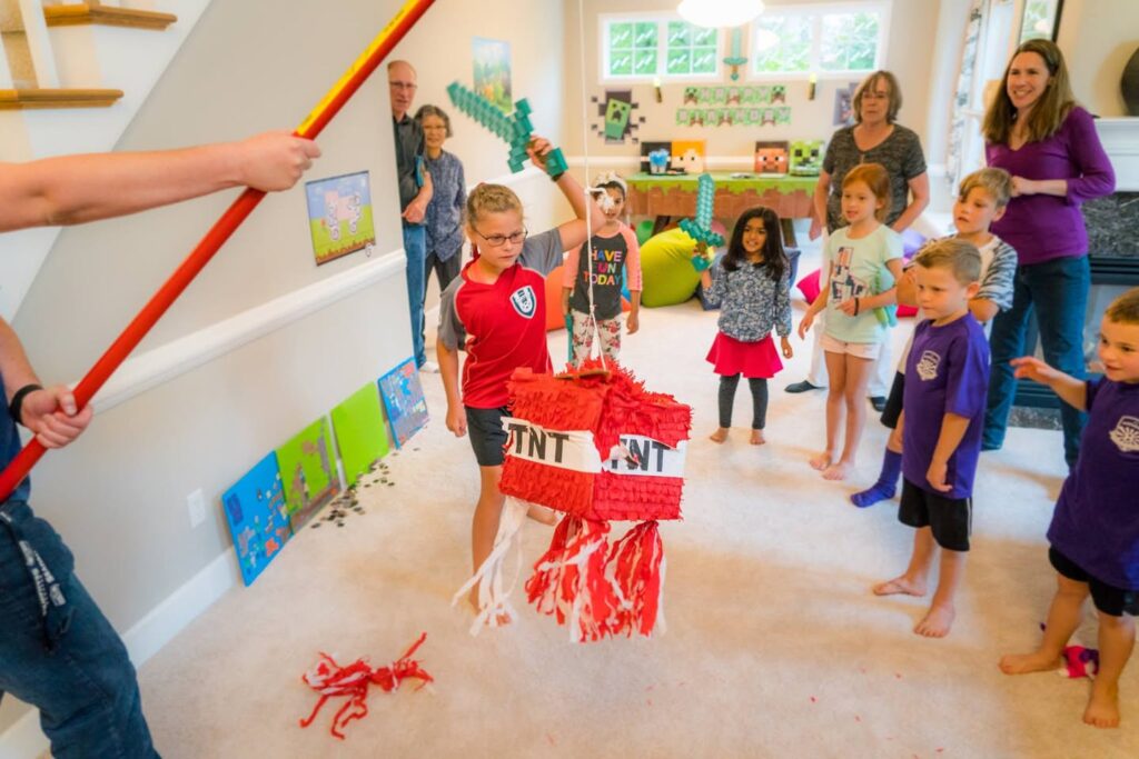 Children and adults in a living room where a child is swinging at a piñata while others watch.