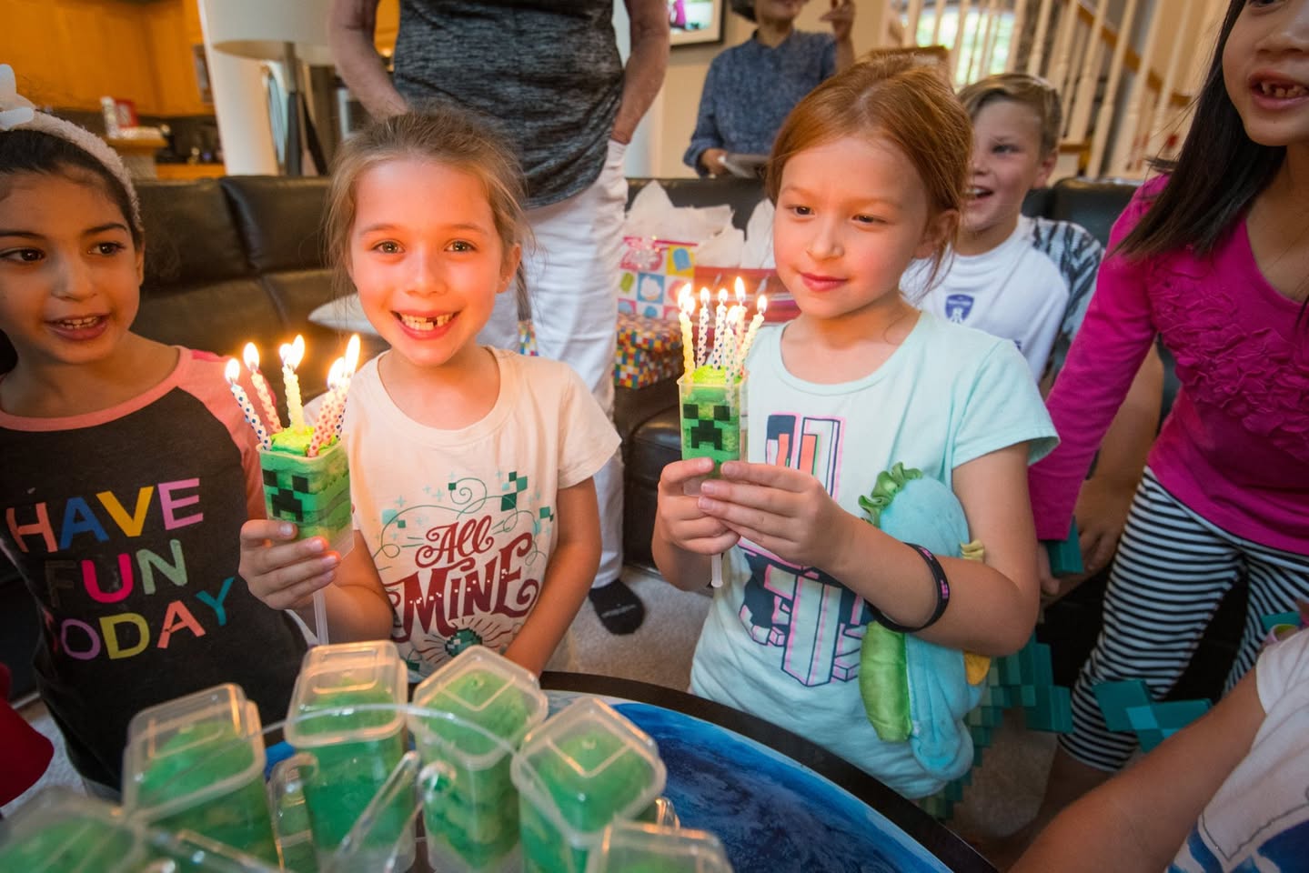 A group of children holding cupcakes with lit green candles at a party.