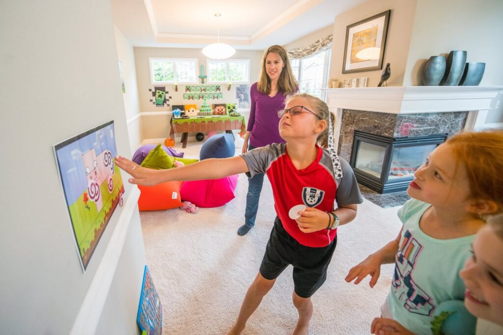 A child plays the Nintendo Wii with a Wii remote in a cozy living room. Other family members watch the screen nearby.