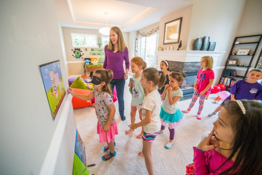 A group of children and an adult are engaged with a colorful wall-mounted game in a bright living room. The kids appear excited and focused on the activity.
