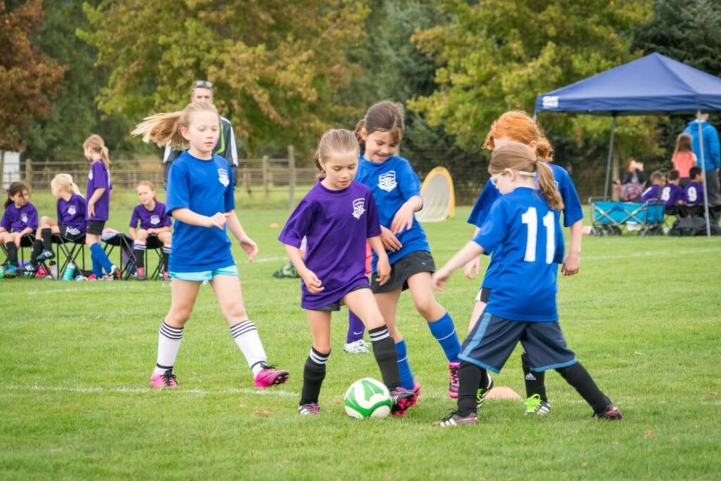 A group of young soccer players in blue and purple uniforms compete on a grass field.