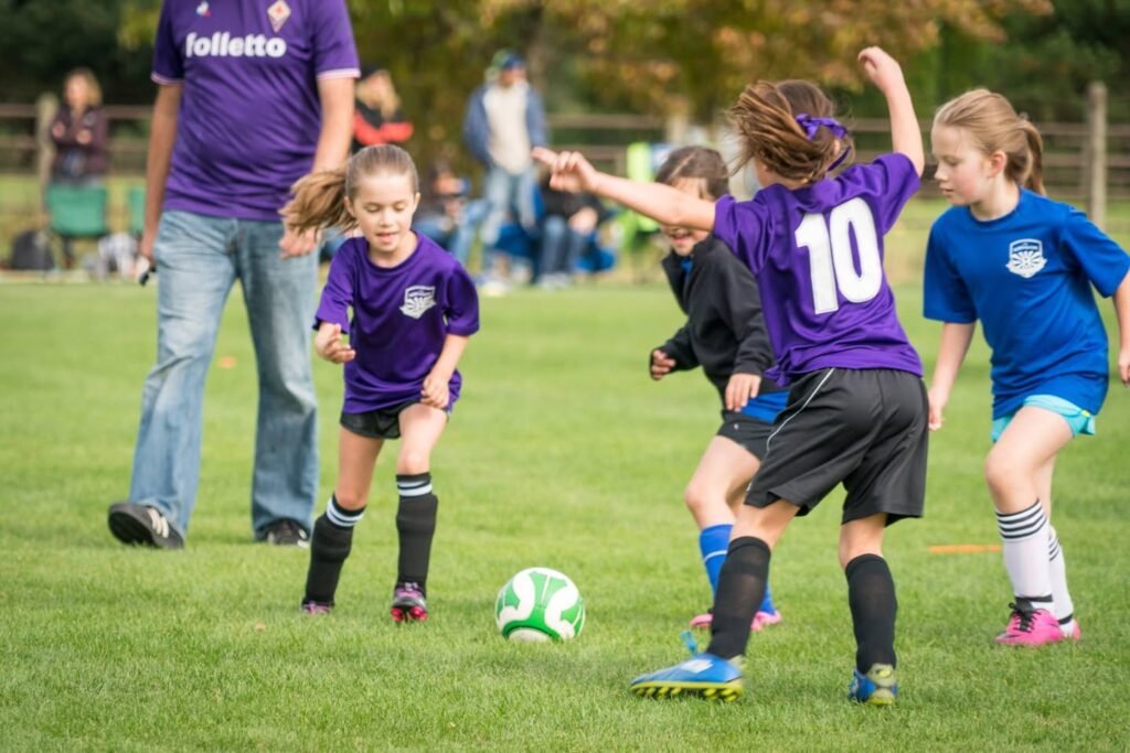 Players in purple and blue jerseys compete for a soccer ball during a youth match.