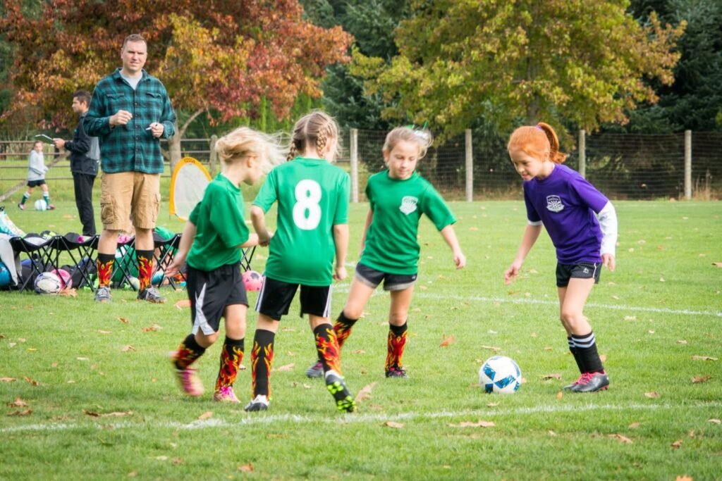 A group of children playing soccer in green and purple jerseys on a grass field in the Pacific Northwest.