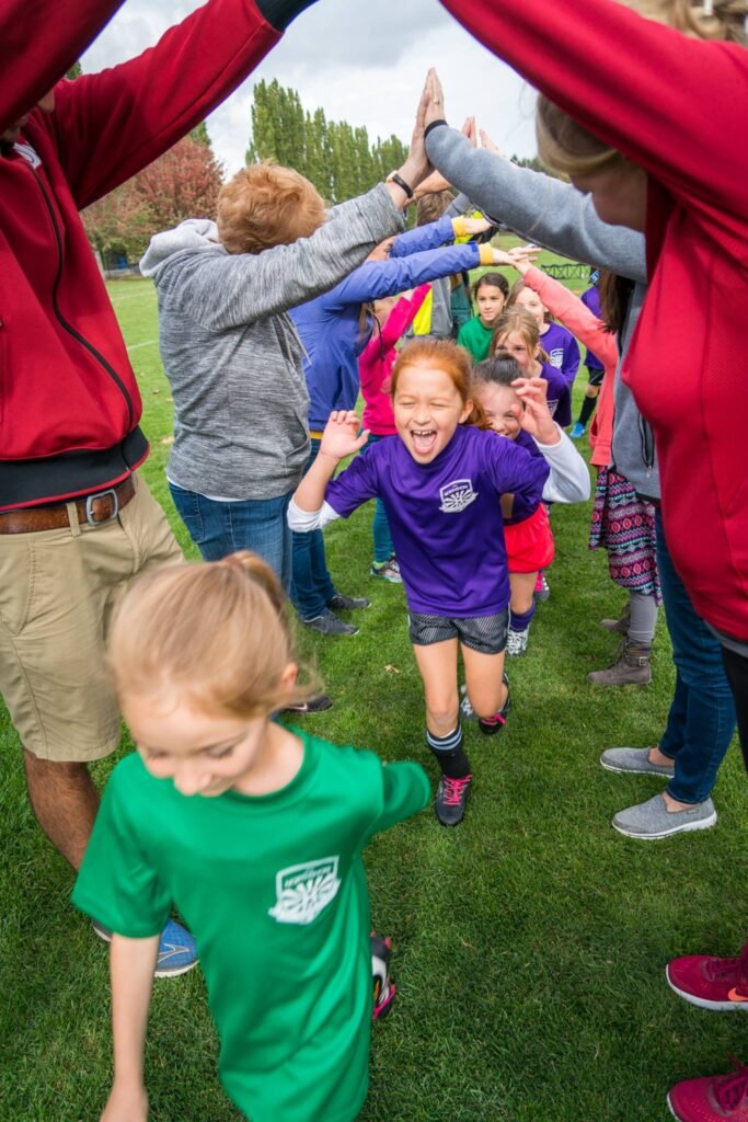 Children high-five as they run under a human canopy at a school event. A joyful and active moment at an outdoor gathering.