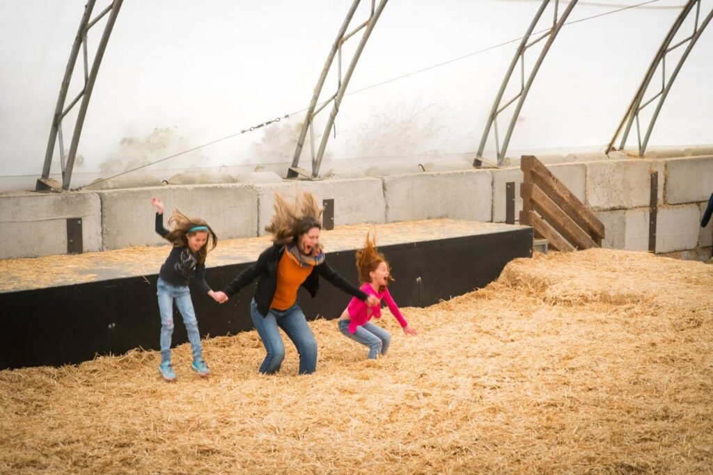 A family running through a hay arena with arched barn structure.