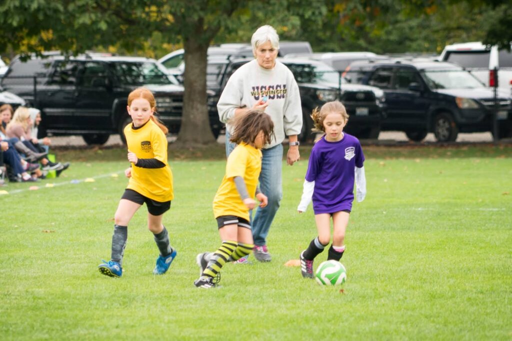 Young athletes in yellow and purple uniforms compete in a youth soccer match on a lush green field.