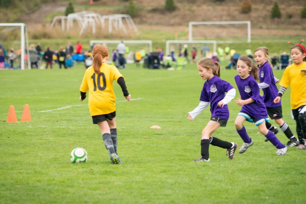 Player in yellow jersey chasing a soccer ball while pursued by players in purple uniforms during a match.