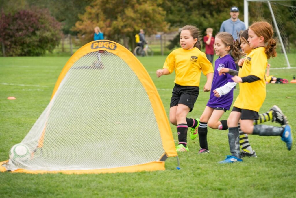 Junior soccer players in yellow uniforms sprinting on a green field.