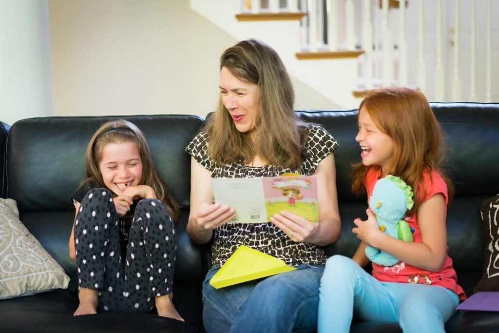 A woman reading a book to two children on a black leather couch in a cozy living room near a staircase.