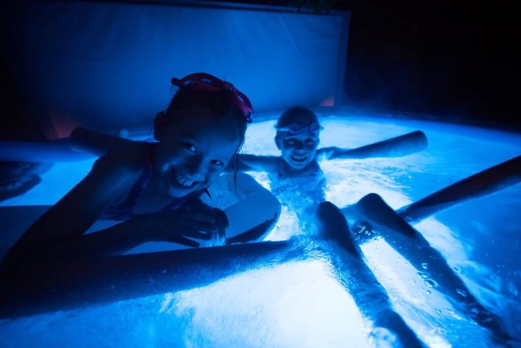 Two individuals enjoying a relaxing evening in a warmly lit spa, with vibrant blue lighting illuminating the water. The setting is cozy and intimate, perfect for unwinding after a long day.