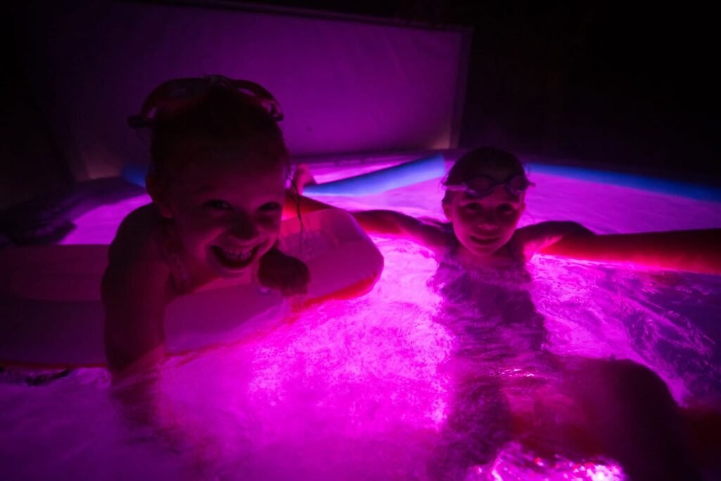 Two people enjoy a hot tub illuminated by vibrant purple lighting.