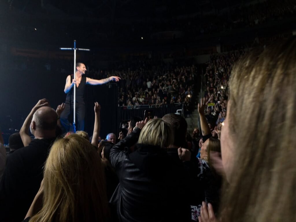 A performer on stage holding a cross while engaging a crowd at a concert.