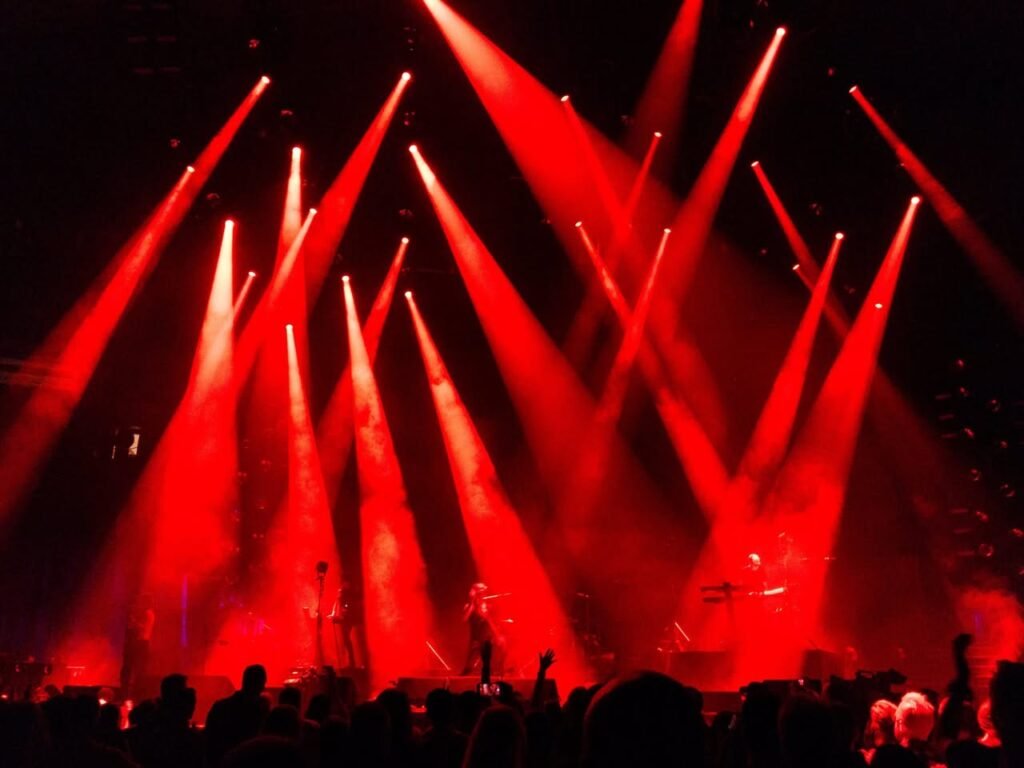 Vibrant red concert spotlights cutting through dark air to illuminate a live music stage.