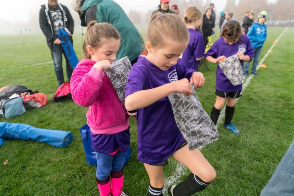 Young children in purple jerseys handle soccer goal nets on a foggy field.