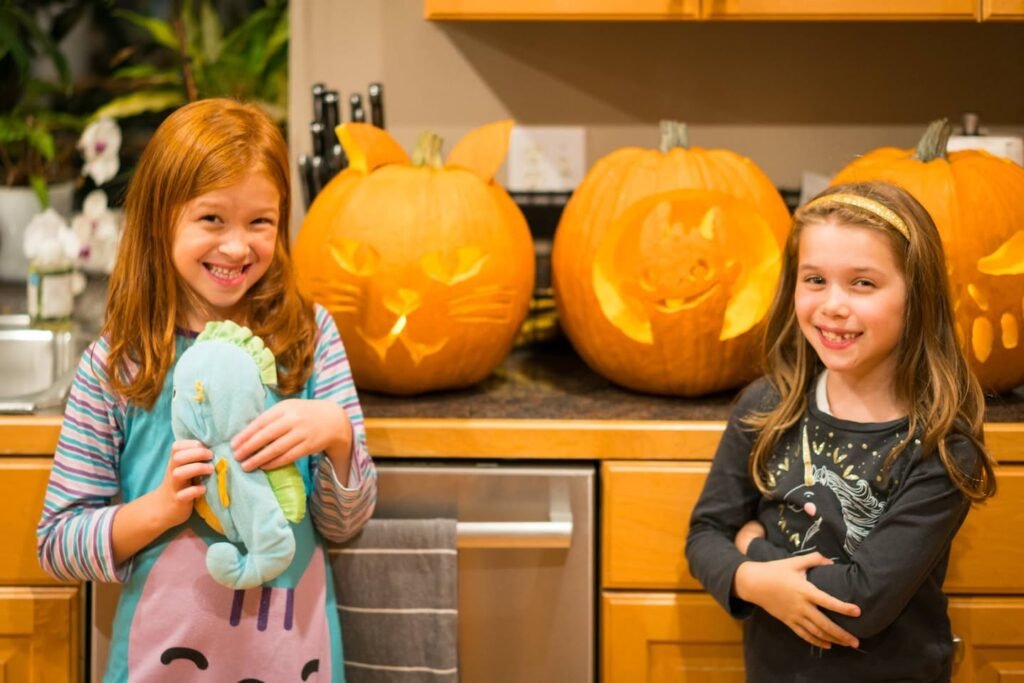 Two children pose with carved pumpkins in a cozy kitchen, capturing the essence of the fall season.