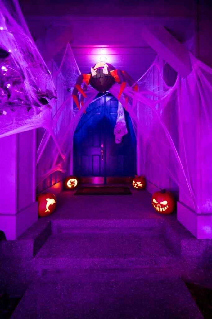 A spooky Halloween front door adorned with cobwebs and glowing jack-o'-lanterns under vibrant purple lights.