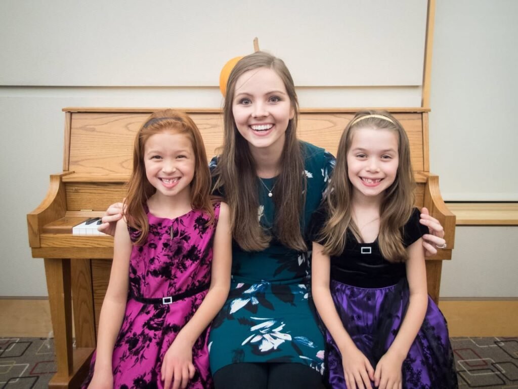 Three girls wearing colorful dresses sit together in a church pew. A wooden pulpit is visible behind them.