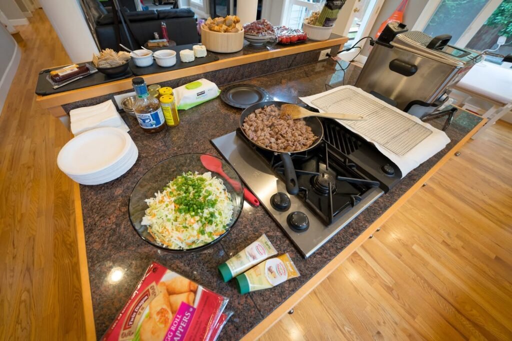 A view of a kitchen island with food ingredients and a stovetop. The counter holds a bowl of salad and a pan of cooked meat.