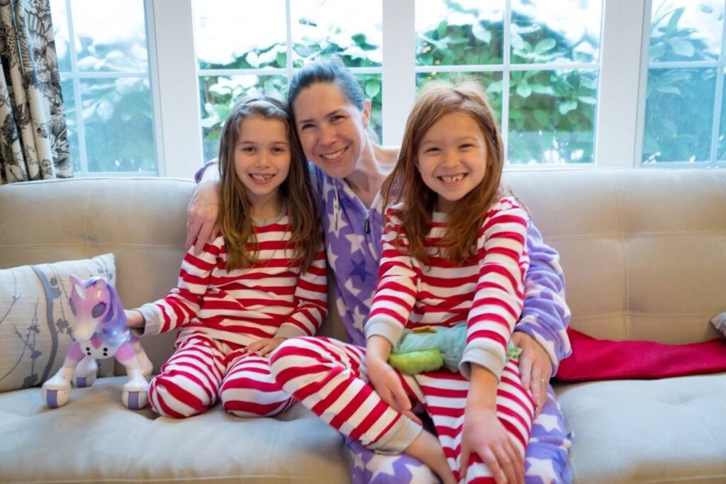 A family in matching pajamas sits together on a beige couch by a bright window, surrounded by festive striped sleepwear and plush pillows.