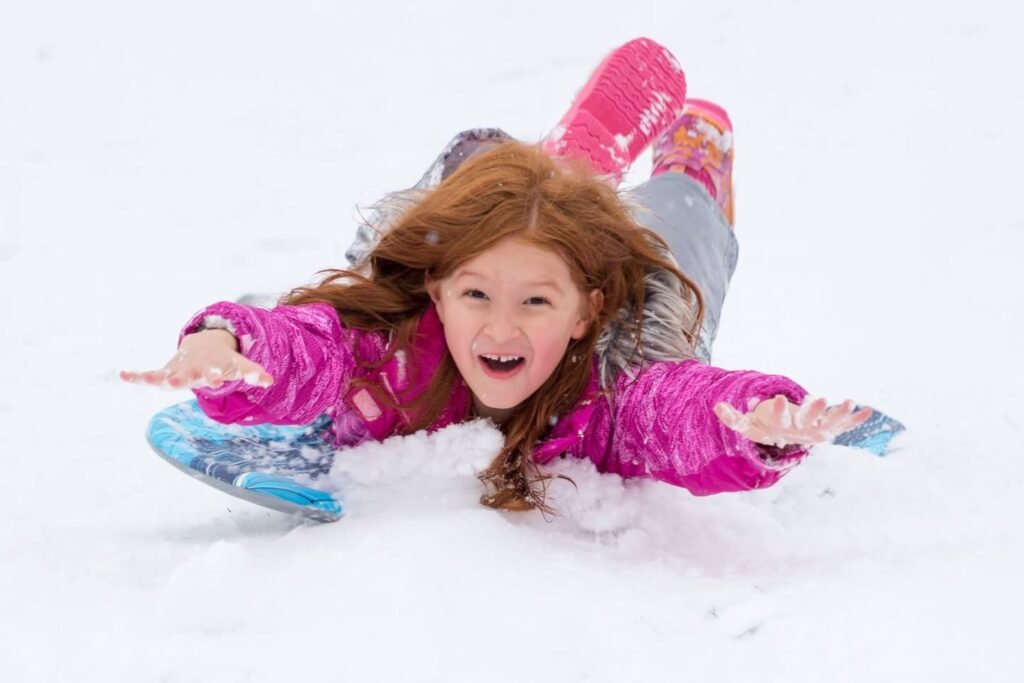 A child enjoying a snowy day while making a huge snow angel in bright pink clothes.