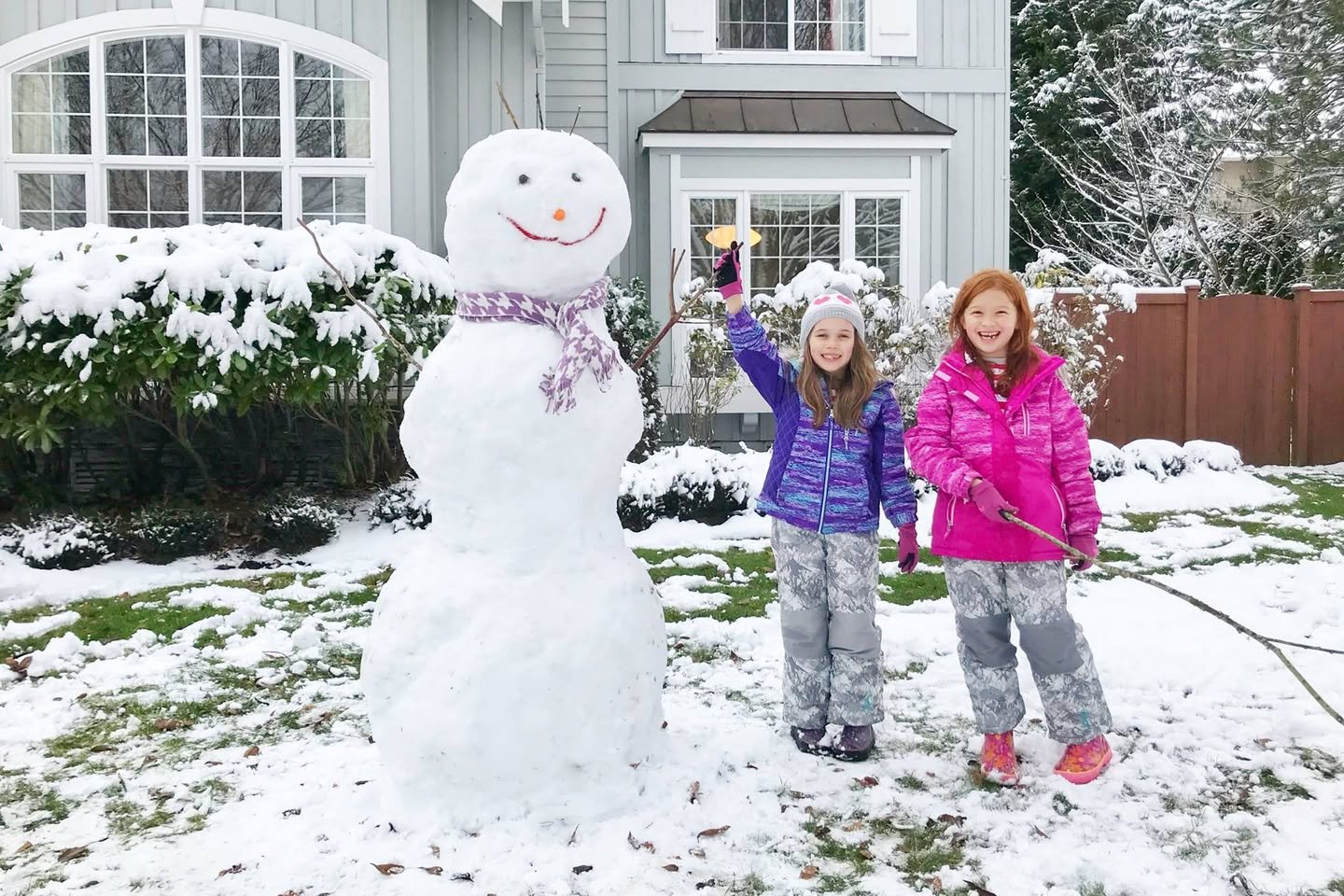 Sledding A happy child and a large snowman in a snowy backyard.