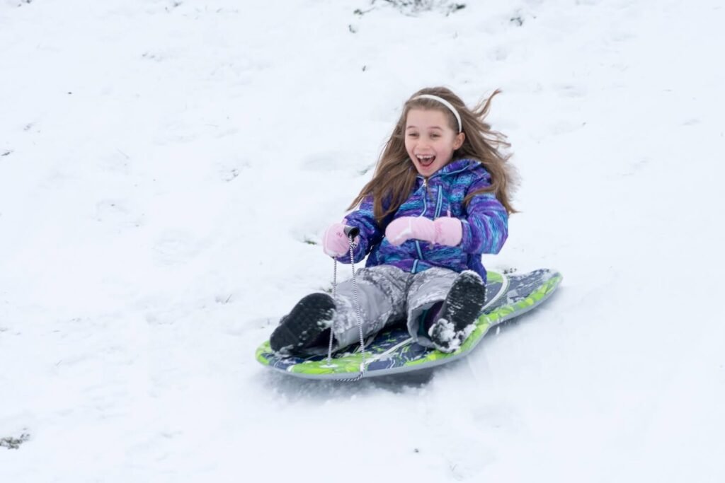 A person enjoying a snowy day by sledding down a hill with a joyful expression.
