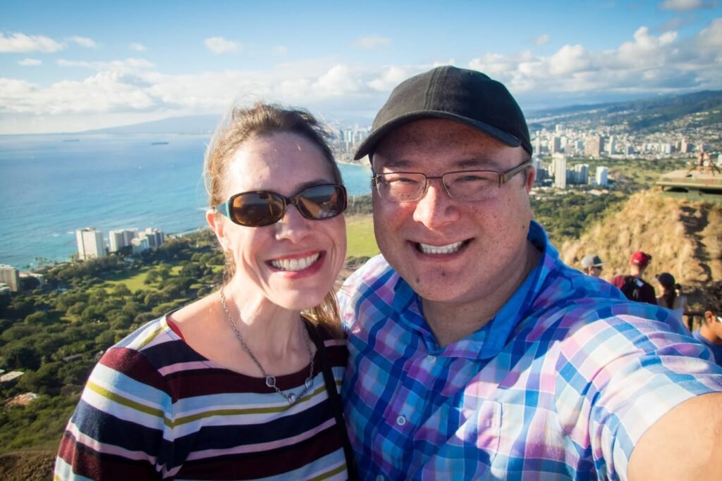 Two travelers taking a selfie with a stunning coastal cityscape in the background, showcasing their love for exploring new places.