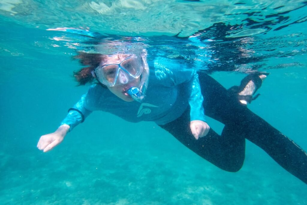 Underwater shots of a person wearing a mask and snorkel swimming in clear water with a sandy bottom.