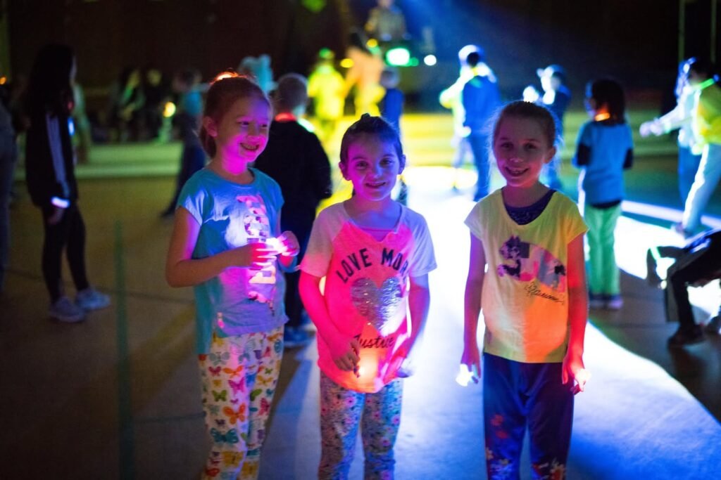 Children are dancing and glowing under black light at a night event.