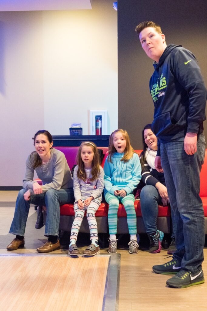 A happy group of people posing for a photo inside a climbing gym. They are seated on a red bench in front of a climbing wall.