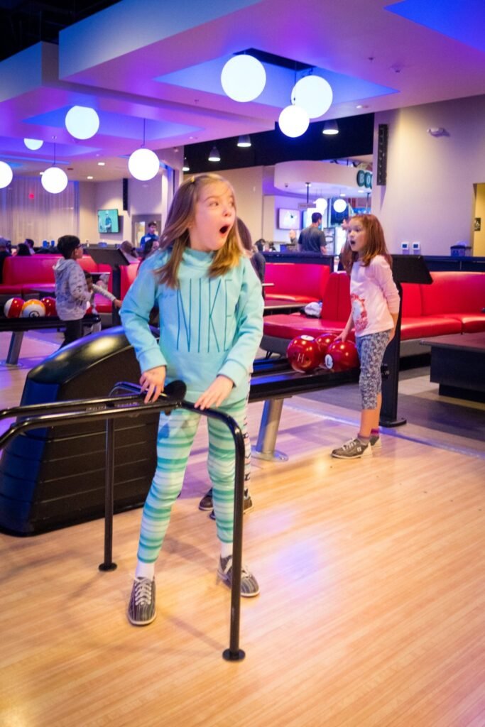 A child practices yoga in a brightly lit modern lounge with colorful seating and decorative spherical lights.