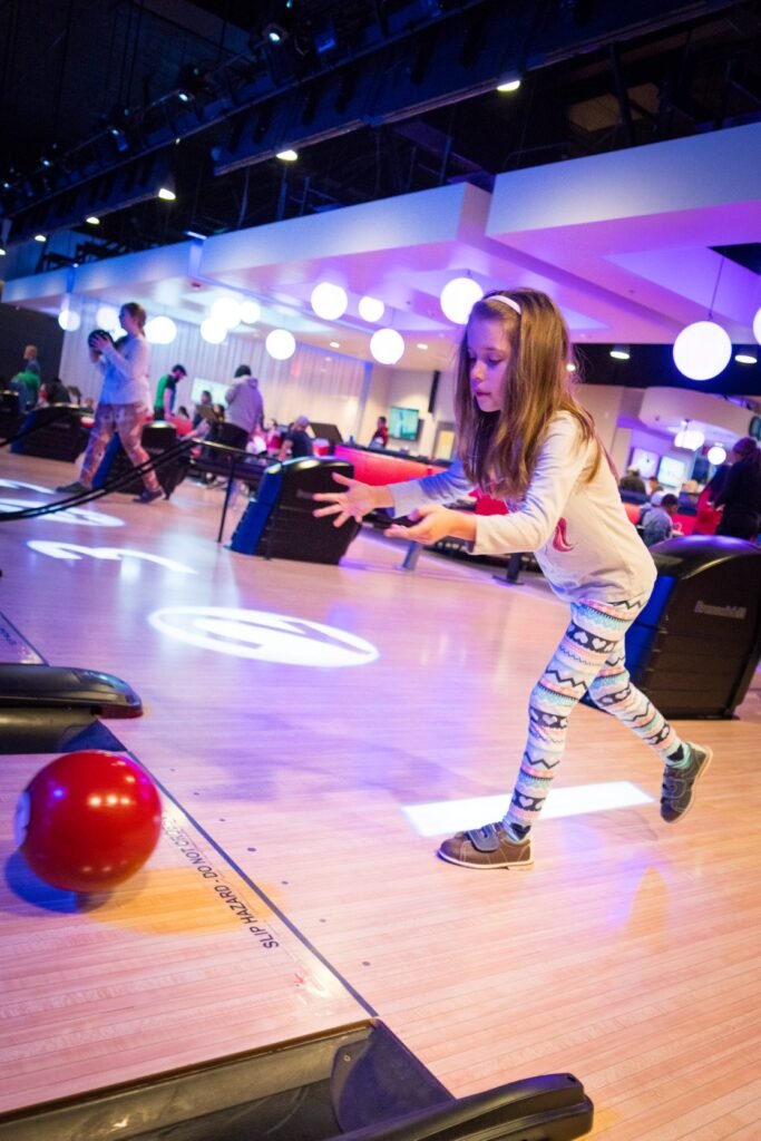 A child playing a virtual bowling game in a lively indoor arcade with vibrant purple lights.