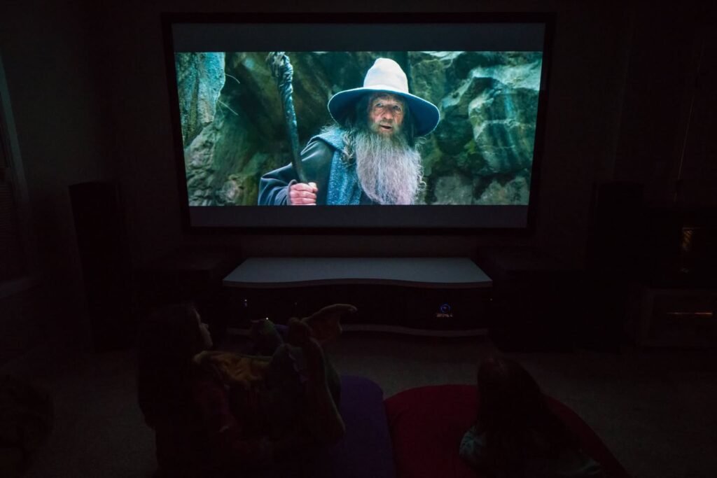 A dark home theater with a projector displaying a scene from a fantasy film featuring a wizard in a wide-brimmed hat.