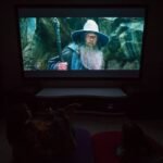 La Push A dark home theater with a projector displaying a scene from a fantasy film featuring a wizard in a wide-brimmed hat.