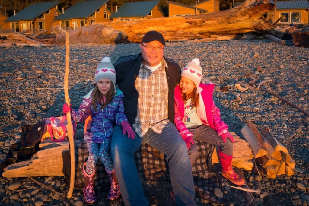 A family of three enjoys a cold day on a sandy beach in the Pacific Northwest. They are bundled up in winter gear by the water's edge.