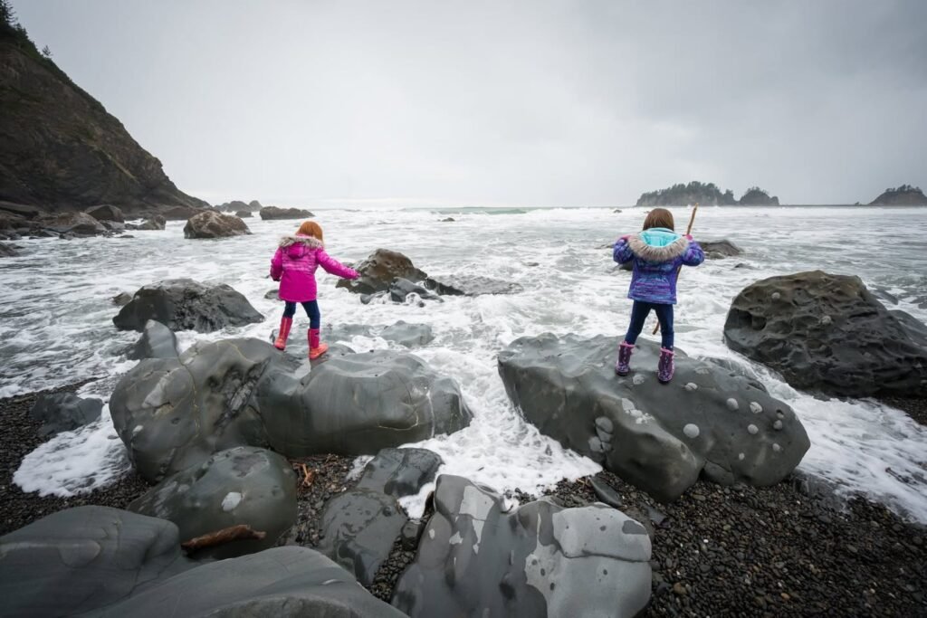 Two people standing on coastal rocks in bright jackets facing the ocean.