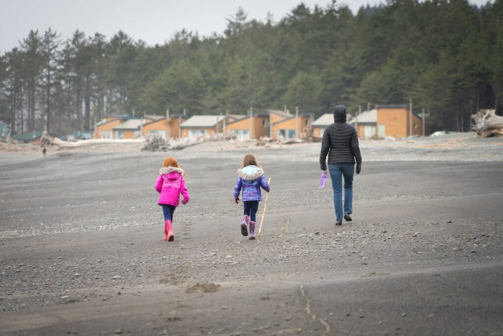 Walking along a sandy shore with pine trees in the distance.